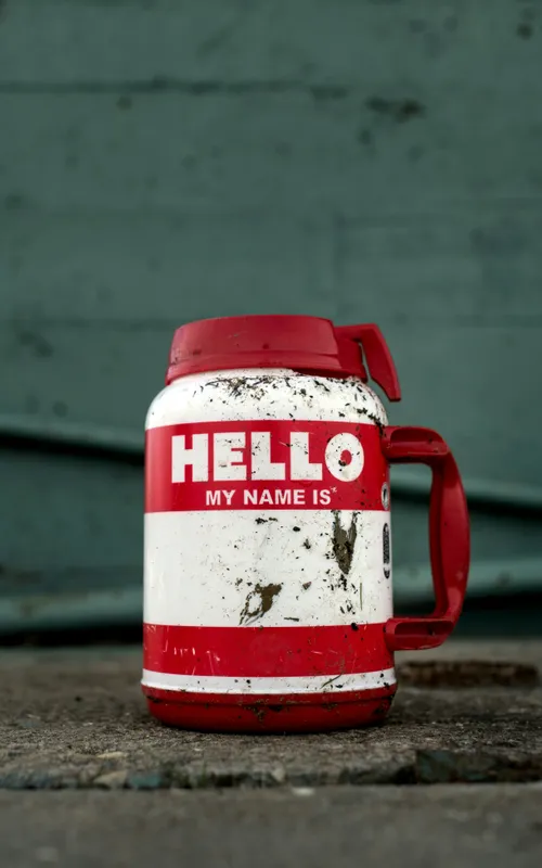 Verbeulter roter Thermobecher mit der Aufschrift 'Hello, my name is' auf einem Pflasterstein